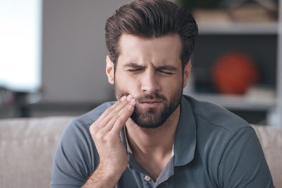 Image of man wincing in tooth pain and hoping to see and emergency dentist.